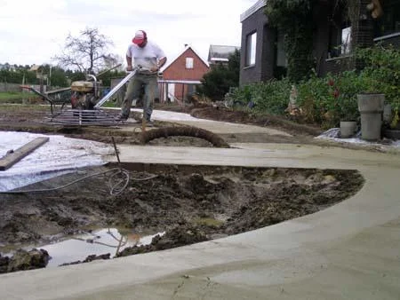 Gebogen zandkleurig betonpad tijdens het polieren in de tuin