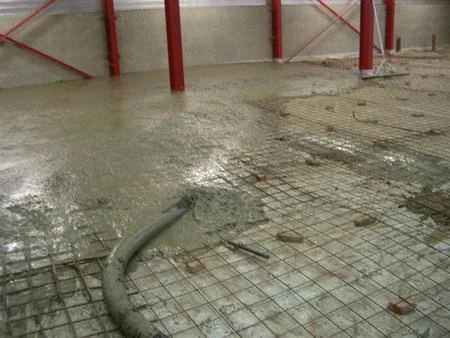 Grijs beton wordt via een pompslang verdeeld op de wapening bij De Coninck