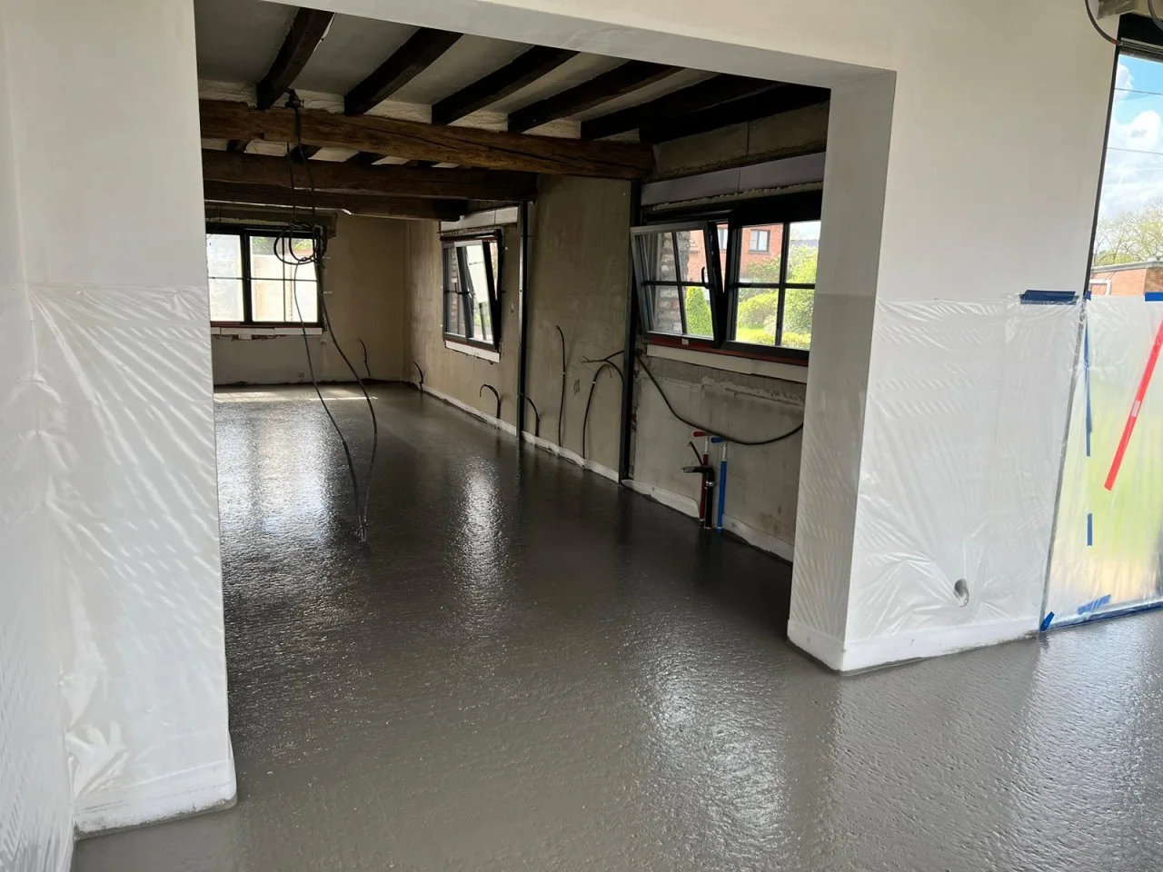 Vers gestorte betonvloer in een woning met afgedekte wanden en houten plafondbalken