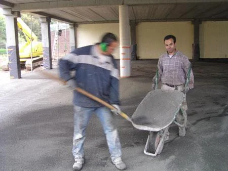 Twee medewerkers met gereedschap en kruiwagen tijdens de vloerwerken in Maaseik