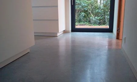 Detail van de grijze betonvloer naast de witte keuken en het tuinraam in Oostmalle